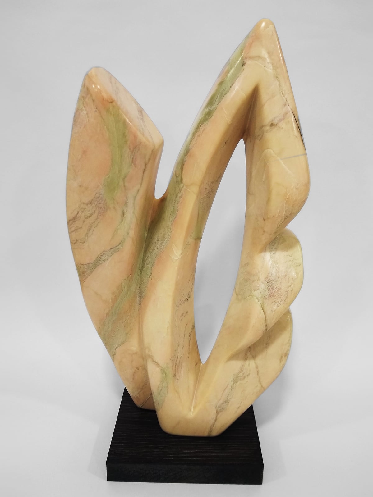 Escultura em mármore claro de veios verdes: duas formas curvas que se abrem deixando um vazado entre elas, sobre base escura